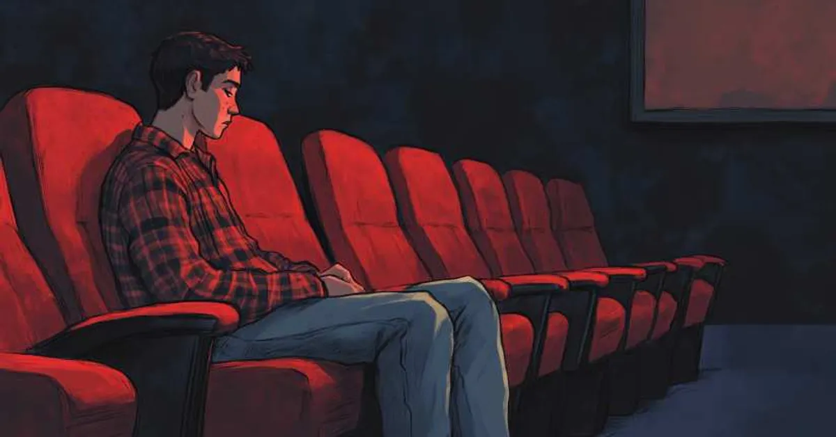 A young man sitting alone in a movie theater surrounded by empty red seats with the dim glow of the screen creating a quiet isolated scene