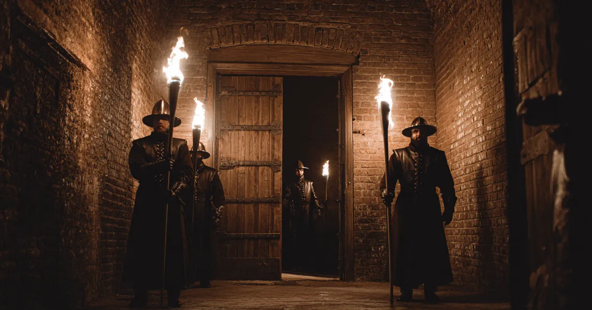 A dungeon corridor with guards holding torches outside a heavy wooden door hinting at hidden danger in Richard III Act 1 Scene 4